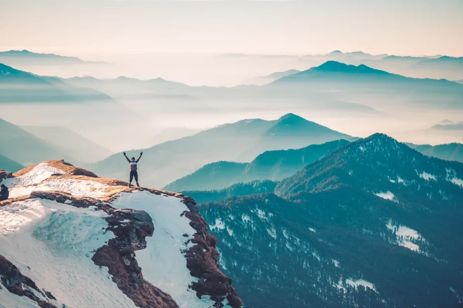 Personne levant les bras au sommet d'une montagne après avoir réussi à changer ses habitudes et atteindre ses objectifs.
